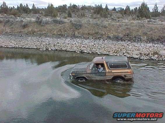 1978 Ford Bronco driving through shallow water with a person inside