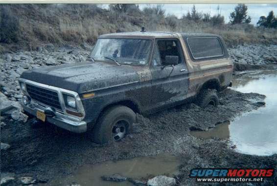 Mud-covered 1978 Ford Bronco stuck in mud and water, front-left three-quarter view
