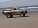 1996 Ford Bronco - A two-tone Ford Bronco is driven on the beach near the ocean waves.