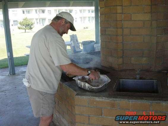 Man cooking at a brick grill with a sink and a Supermotors.net watermark