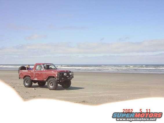 Red pickup truck with off-road tires and a spare tire on the back, parked on a sandy beach