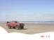 1996 Ford Bronco - A red pickup truck with off-road modifications sits on a beach with the ocean in the background.