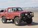 1996 Ford Bronco - A red off-road truck with large tires is parked on a beach, with text on the side indicating it belongs to the "2 BIG BRONCOS 4X4 CLUB".