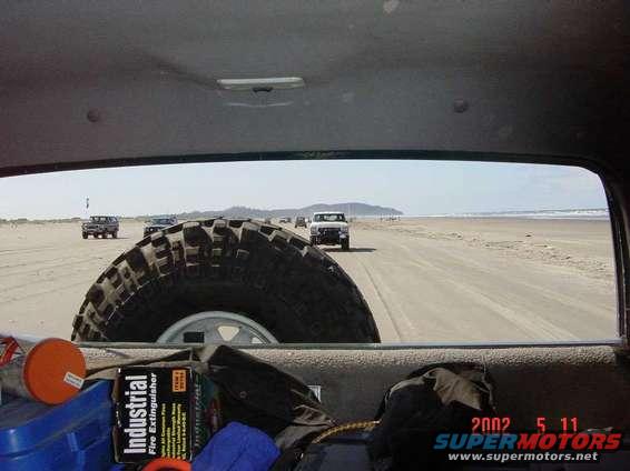 View from inside a vehicle looking out at other vehicles driving on a sandy beach near the ocean