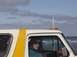 1996 Ford Bronco - A woman sticks her tongue out from the interior of a white and yellow SUV, with the ocean visible behind. A watermark indicates the photo w…