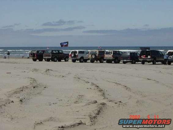 Several SUVs parked in a line on a sandy beach with the ocean in the background