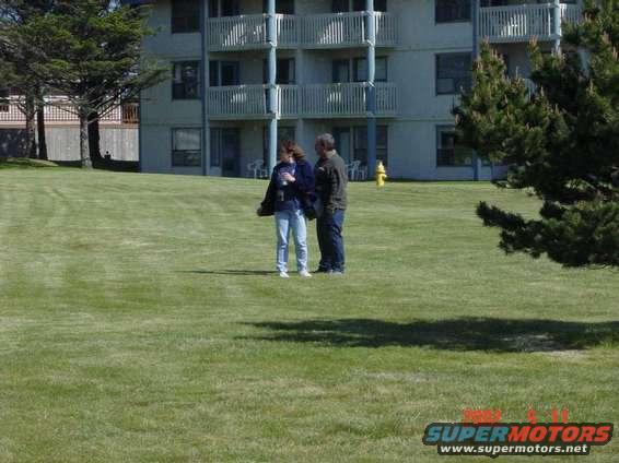 Two people stand on a grassy lawn in front of a multi-story building with balconies