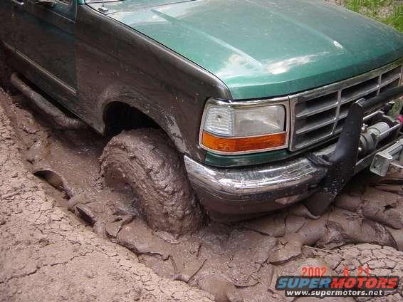 1996 Ford Bronco stuck deep in mud, front tire submerged. Winch visible on bumper