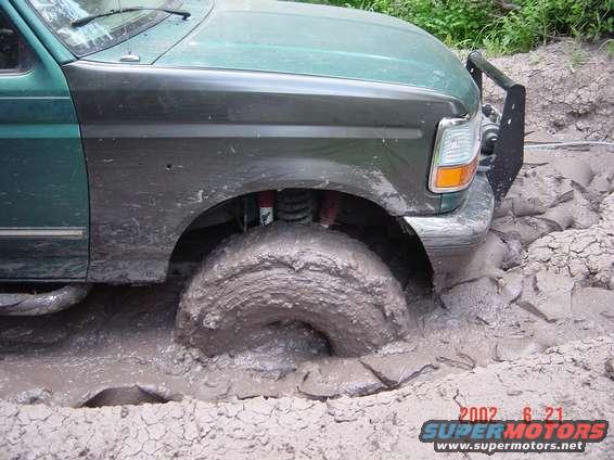 Green 1996 Ford Bronco with large tires stuck deep in mud, front right wheel submerged