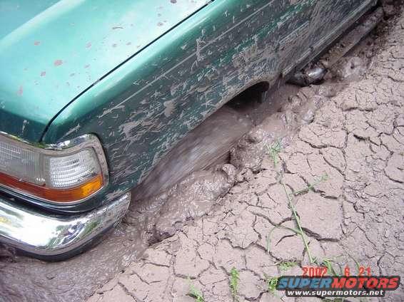 Green SUV stuck in mud, front fender and wheel visible