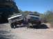 1979 Ford Bronco - Two Ford trucks, a white Bronco and a silver model, navigate a challenging rocky off-road course under a clear blue sky.