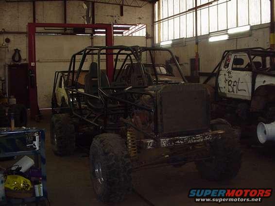 Custom off-road vehicle with roll cage, front view, in a workshop