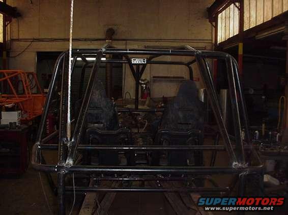 Roll cage and two bucket seats inside a workshop, with another orange frame visible in the background