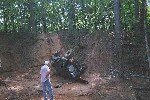 Wrecked dark SUV overturned on a dirt embankment with trees in the background