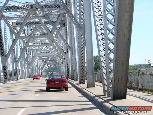 Red 1991 Ford Probe driving on a bridge, rear view