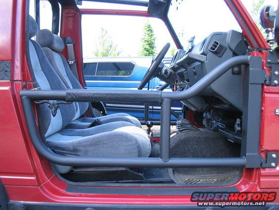 Red Suzuki Samurai interior with grey striped seats, roll cage, and dashboard. Bull skull ornament on seat