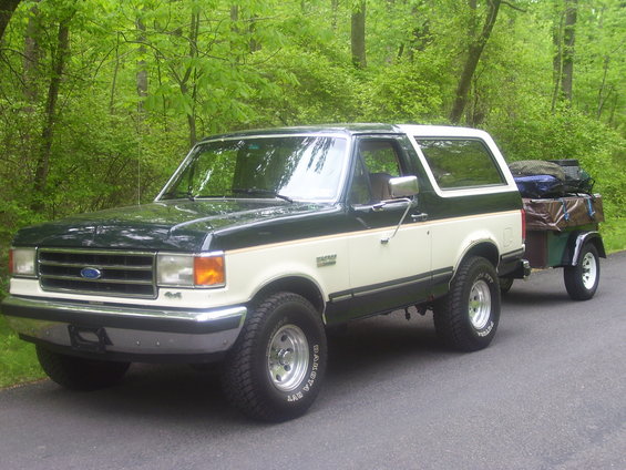 Two-tone green and white 1991 Ford Bronco towing a small trailer loaded with luggage