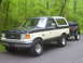 1991 Ford Bronco - A two-tone green and white 1991 Ford Bronco is parked on a paved surface, towing a trailer filled with bags.