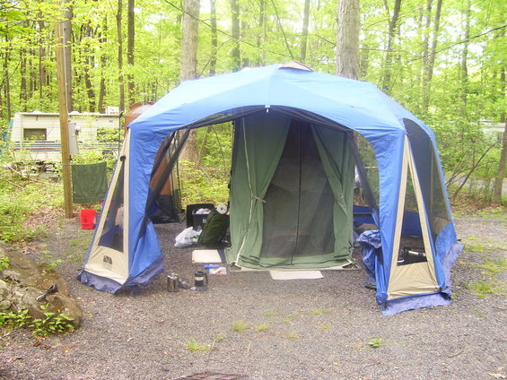 Campsite with a large blue and tan tent structure, a green inner tent, and an RV in the background
