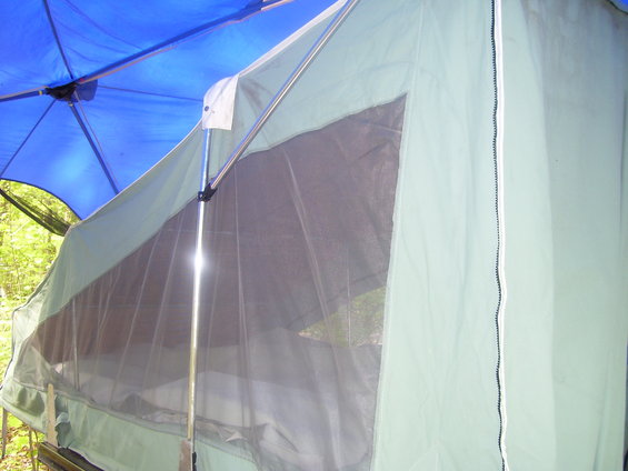 Tent trailer with a blue canopy overhead, showing a mesh window and green fabric