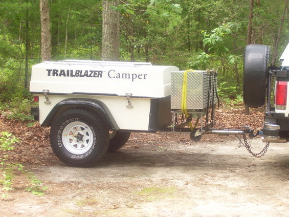 White Trailblazer Camper trailer with diamond plate storage box and spare tire mounted on a tow vehicle