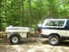 1991 Ford Bronco - 1991 Ford Bronco towing a Trailblazer camper trailer in a forest setting.