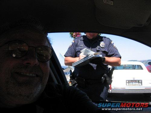 Police officer writing a ticket next to a white car. Man in foreground