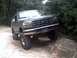 1996 Ford Bronco - A dark green Ford Bronco navigates a rocky trail, its lifted suspension evident as it goes over an obstacle.