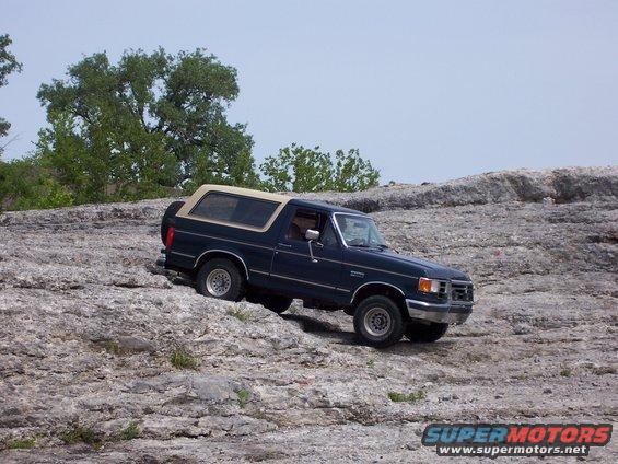 Dark blue 1991 Ford Bronco with a tan top driving on rocky terrain