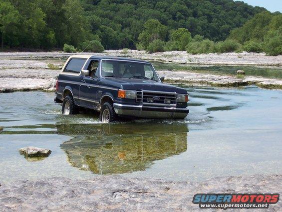 Dark blue 1991 Ford Bronco driving through shallow water