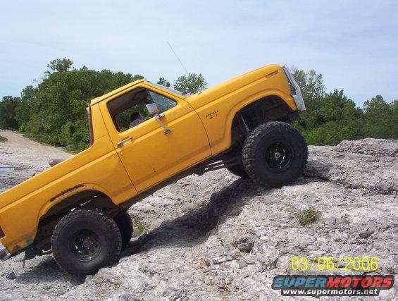Yellow Ford Bronco climbing over rocks, front passenger side visible