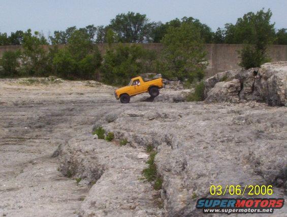 Yellow pickup truck with a short bed driving over rocks