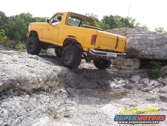 Yellow SUV climbing over rocks on a trail. Driver is visible