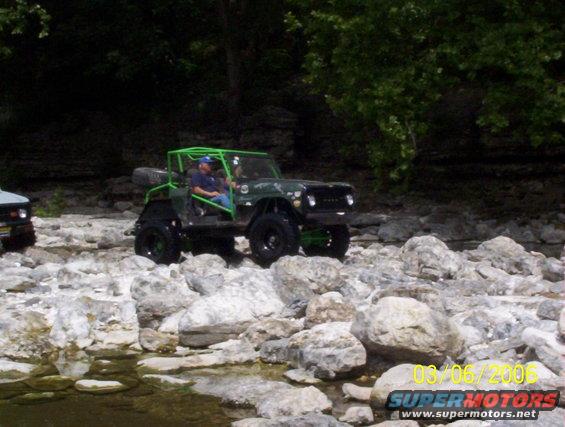 Green 1991 Ford Bronco with a roll cage driving over rocks