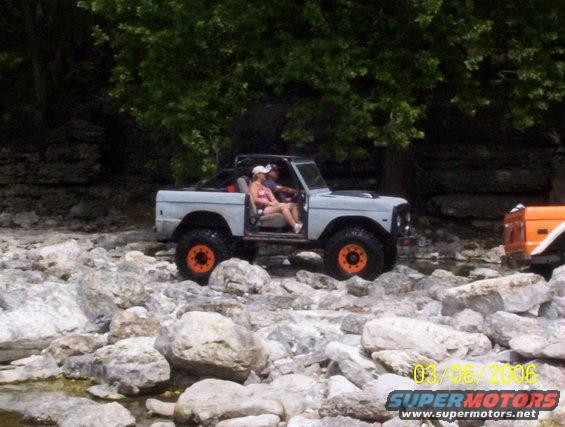 1991 Ford Bronco navigating rocky terrain with passengers. Another orange vehicle is partially visible