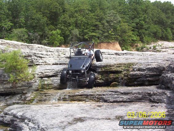 Black off-road vehicle with roll cage navigating rocky terrain with water