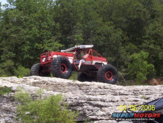 Red and white off-road buggy with large tires on rocky terrain