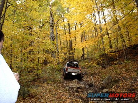 1990 Ford Ranger driving off-road on a rocky, wooded trail during autumn