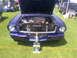 1965 Ford Mustang - A purple 1965 Ford Mustang coupe is displayed with its hood open and a trophy placed before it on a grassy field.