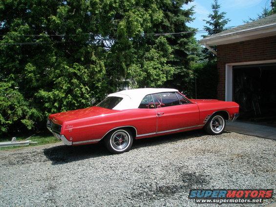 Red 1966 Buick Skylark convertible with a white top parked on a gravel driveway
