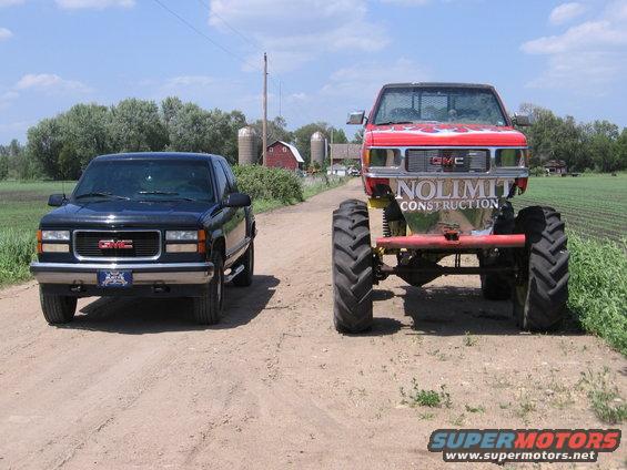 Black GMC pickup truck and a red monster truck with 'NOLIMIT CONSTRUCTION' on the tailgate, parked on a dirt road