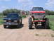 1995 GMC Sierra 1500 - Two GMC trucks, one standard and one monster truck, sit on a dirt road with a farm in the background.