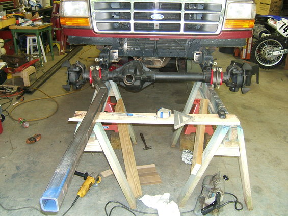 Red Ford truck front end with axle assembly on sawhorses, grille visible