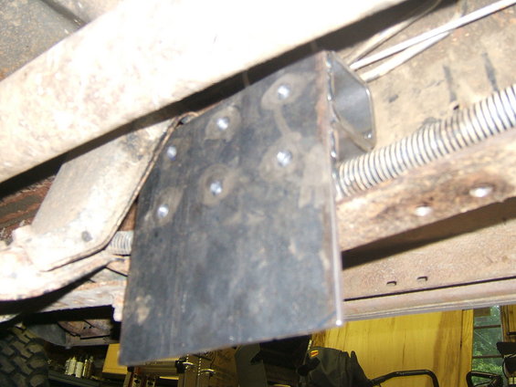 Custom metal bracket bolted to rusty vehicle frame, with visible tire tread and suspension components