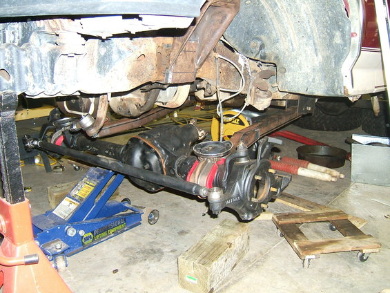 Front axle and suspension parts with red and black accents, on jacks