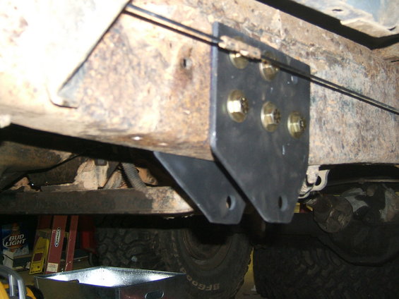 Aftermarket bracket bolted to rusty frame rail with visible brake lines