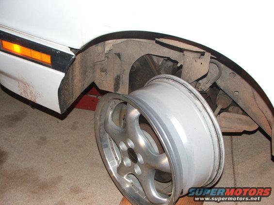 Car's front wheel removed, showing the fender and suspension components. A SuperMotors logo is visible