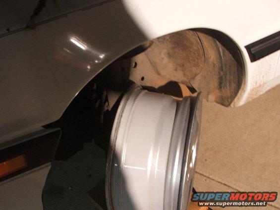 Close-up of a car's wheel well with a white rim leaning against it