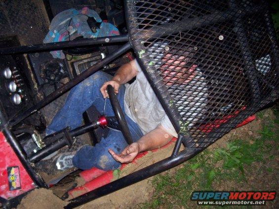 Driver in jeans and t-shirt sits in a roll cage, holding the steering wheel of an off-road buggy