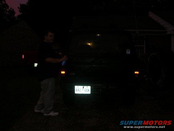 Man holding a spray can next to the rear of a dark SUV with license plate 842-GDK